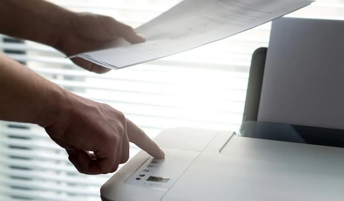a man holding a sheet of paper and pressing a printer button
